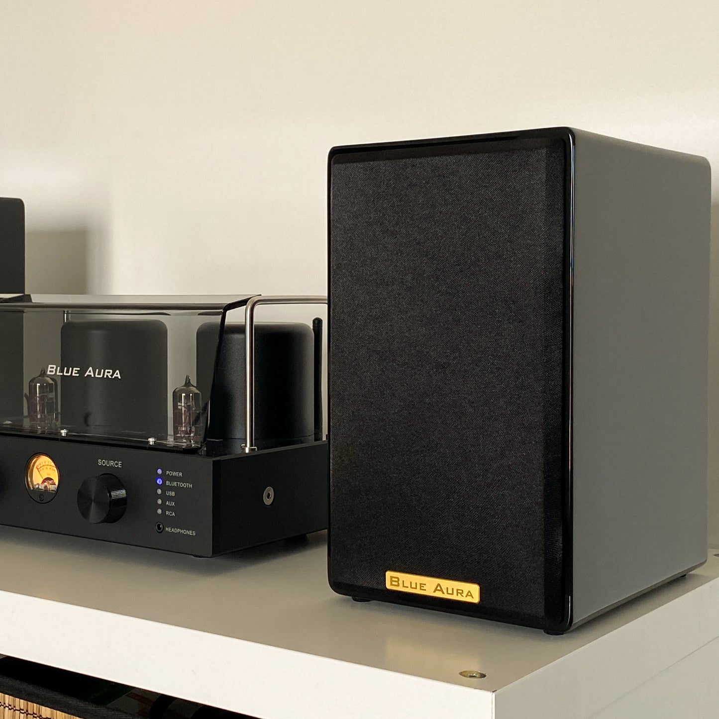 Close-up of the black AT700 right speaker with its fabric grille on, positioned next to the turned-on v50 valve amplifier.