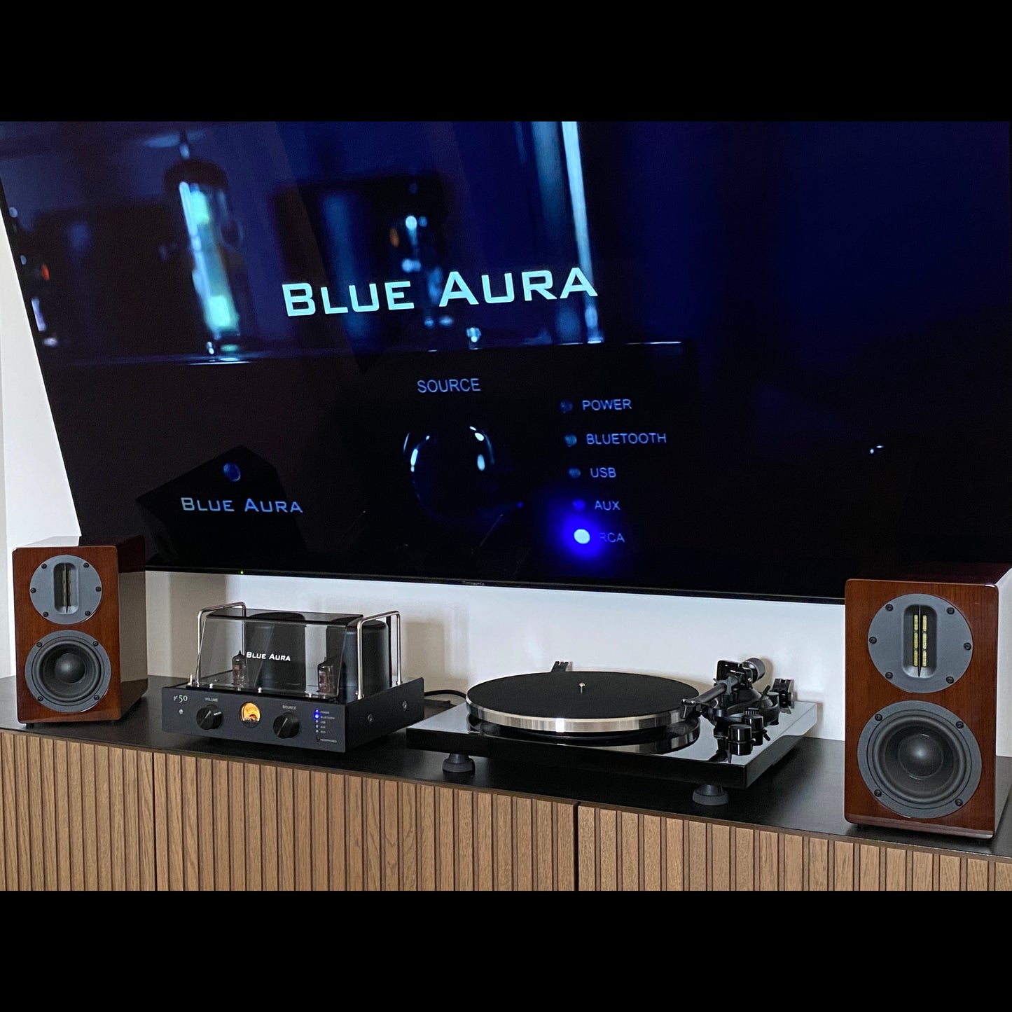 Front view of the Blue Aura Soul Prestige Hi-Fi system with the turned-on amplifier placed on a cabinet under the TV.
