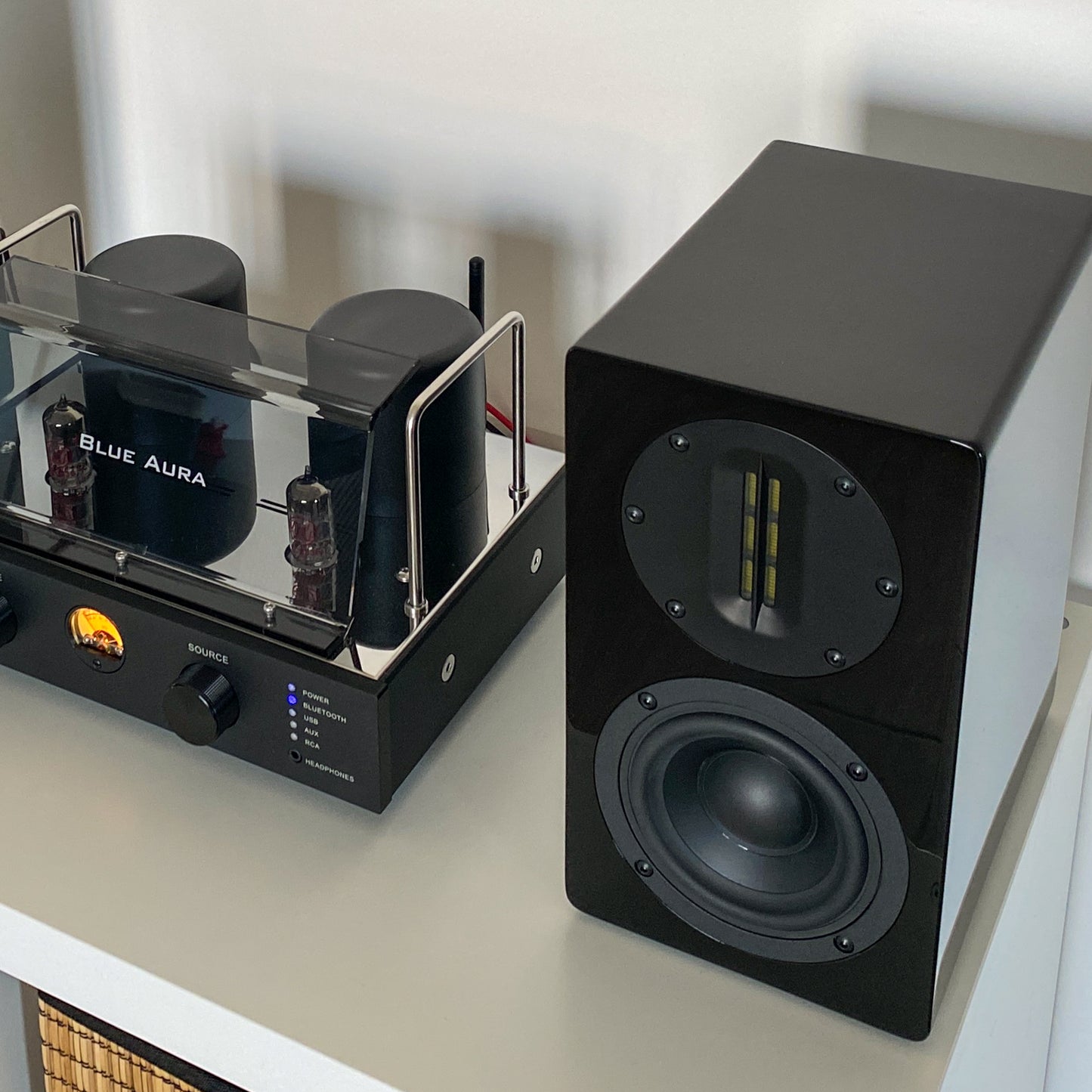 Close-up of the black right AT700 speaker without front grille, highlighting the high-tech AMT tweeter, with the v50 amplifier alongside.