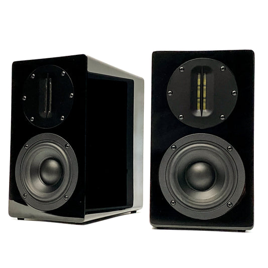Official studio shot of a pair of Blue Aura AT700 compact bookshelf speakers without their grilles, showcasing one from the front and one from a three-quarter profile to highlight the 8-coat high-gloss piano black lacquer finish, AMT tweeters, and paper cone drivers.