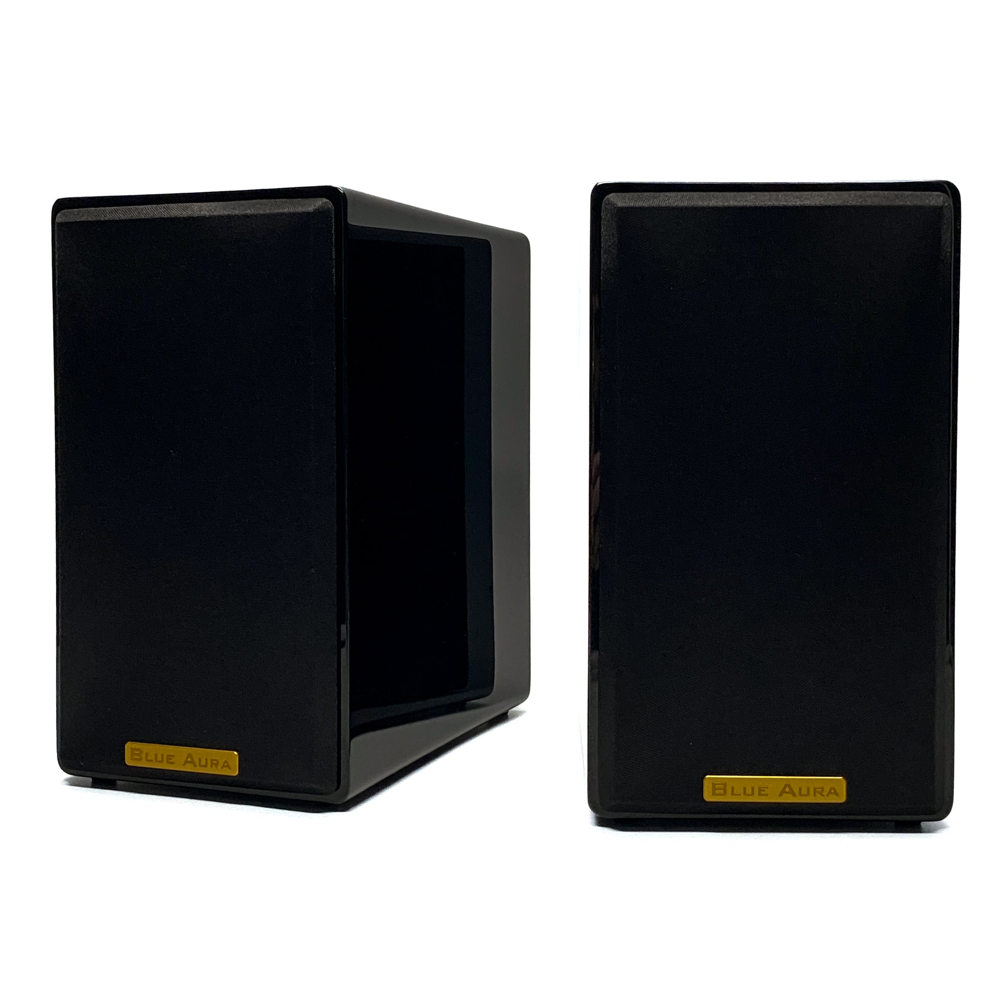Official studio shot of a pair of Blue Aura AT700 compact bookshelf speakers with their black fabric protective grilles, showcasing the elegant gold metallic brand badges and high-gloss piano black finish.