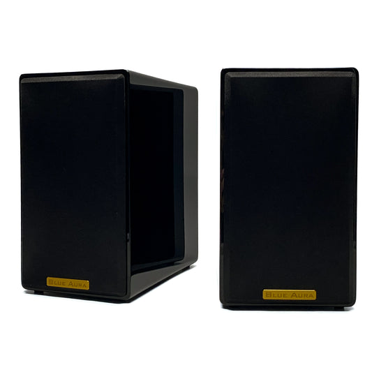 Official studio shot of a pair of Blue Aura AT700 compact bookshelf speakers with their black fabric protective grilles, showcasing the elegant gold metallic brand badges and high-gloss piano black finish.