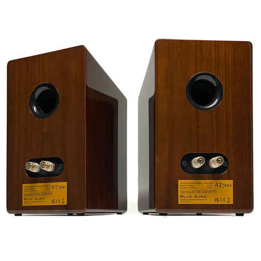 Official straight rear studio view of a pair of Blue Aura AT700 compact bookshelf speakers in premium high-gloss Walnut finish, showcasing the circular bass reflex ports and terminal backplates.