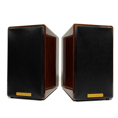 Balanced straight front studio view of the pair of Blue Aura AT700 compact bookshelf speakers, showcasing the stunning mirror-like reflection on their premium lacquer Walnut finish with the fabric grilles on.