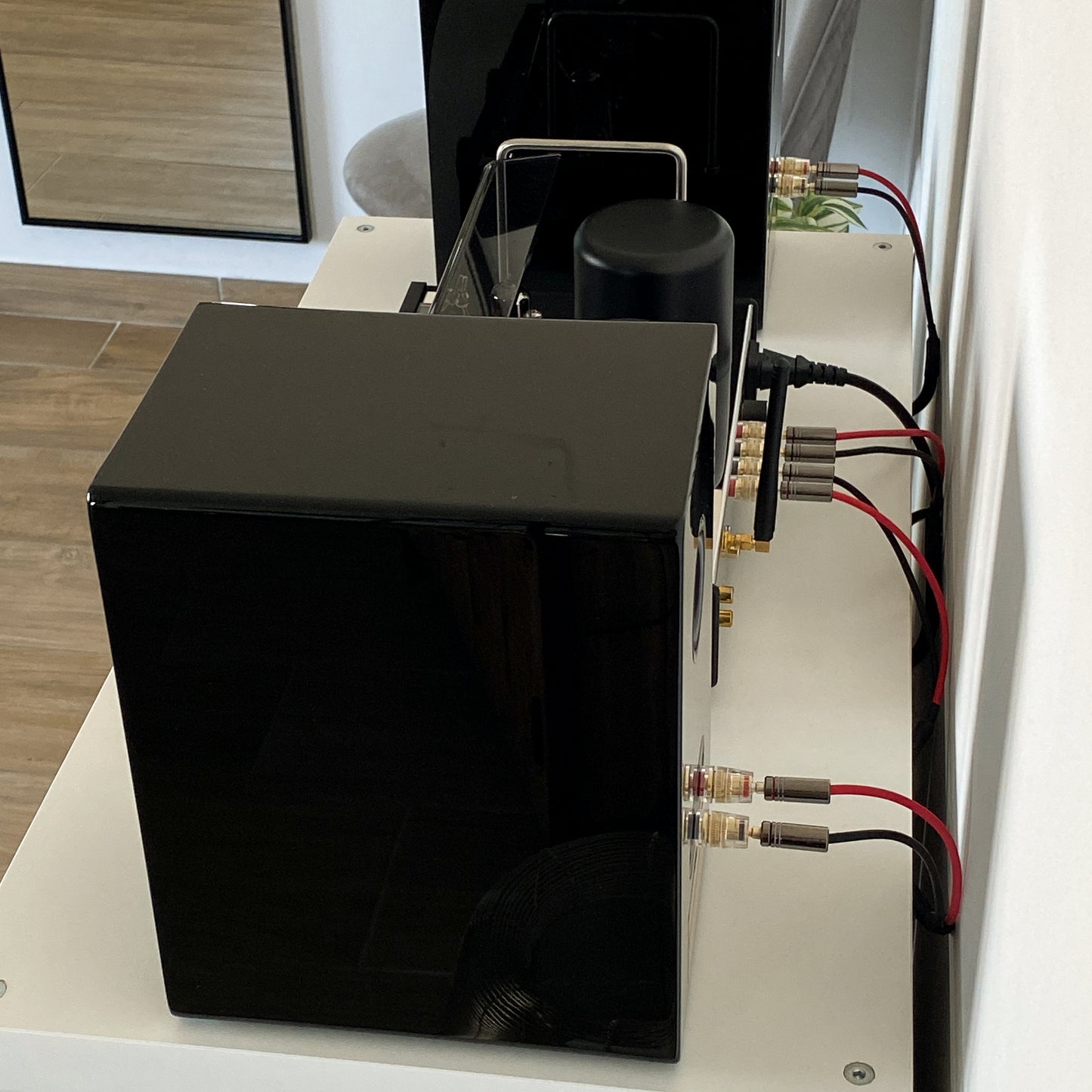 Rear view of the black AT700 speaker with a high-gloss piano finish reflecting a gold candle holder on the floor.