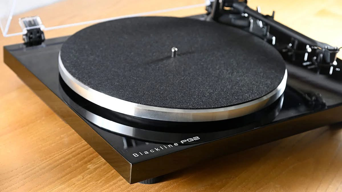 Official high-angle close-up view of the Blue Aura Blackline PG2 turntable, highlighting the elegant white model logo printed on the corner of the premium high-gloss black plinth.