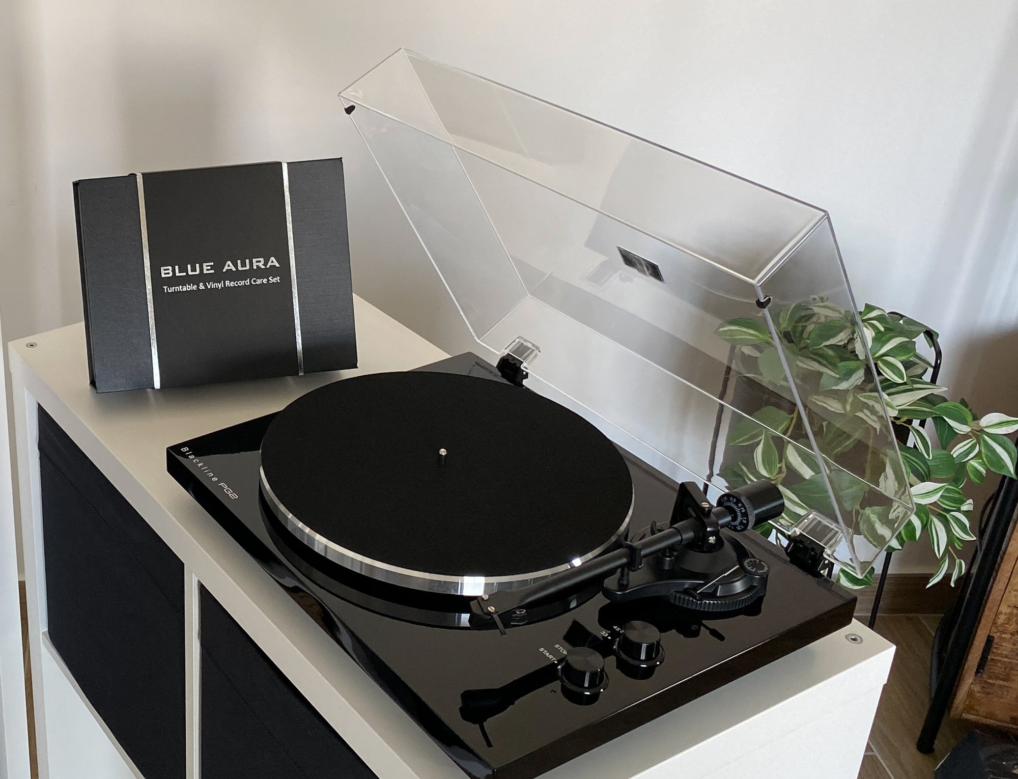 High-angle top lifestyle view of the Blue Aura Blackline PG2 Hi-Fi turntable on a white cabinet with its clear dust cover open.