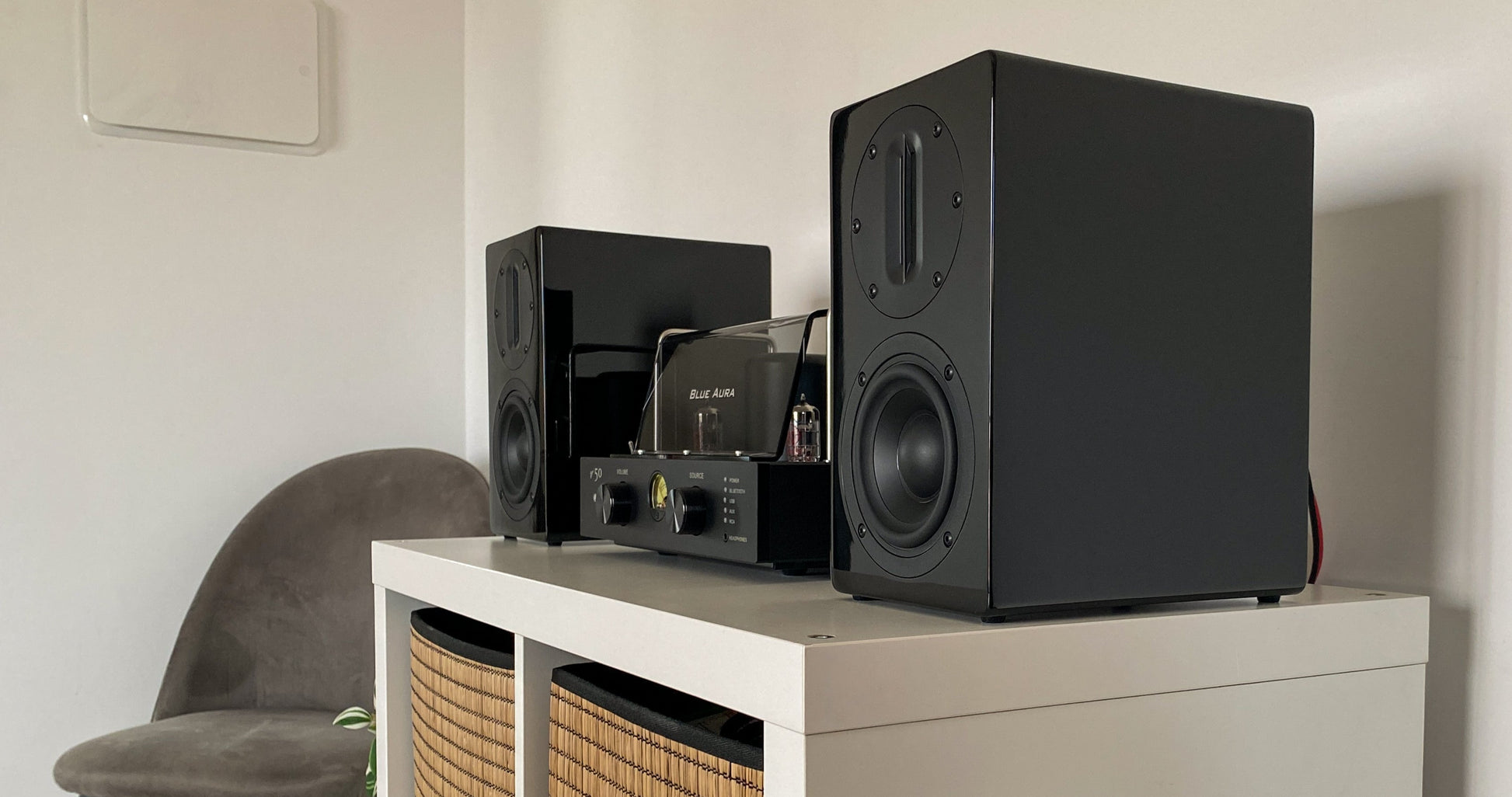 Blue Aura v50 Hi-Fi system with its black AT700 speakers set up on a white cabinet.
