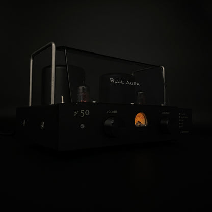 Front view of the Blue Aura v50 hybrid amplifier in the dark, highlighting its illuminated warm-glow VU meter.
