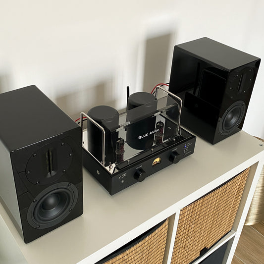 Close-up top-down view of the v50 amplifier and black AT700 speakers from the Blue Aura stereo system.