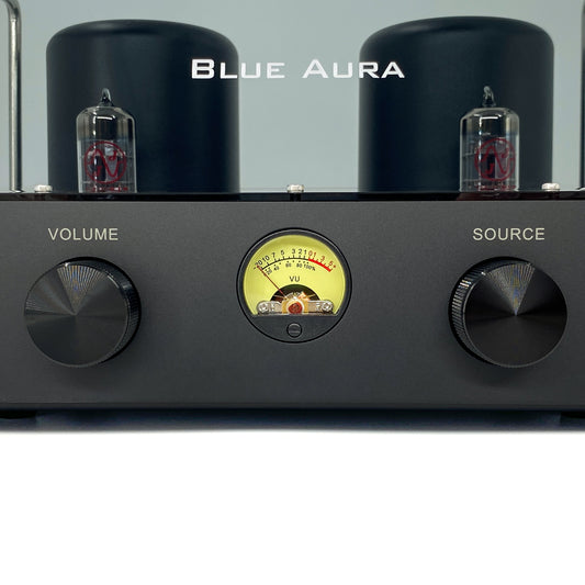 Official macro close-up front view of the Blue Aura v50 hybrid valve amplifier at rest, focusing on the circular yellow VU meter balanced between the dual black aluminium control knobs, with JJ Electronic ECC83 vacuum tubes visible behind.