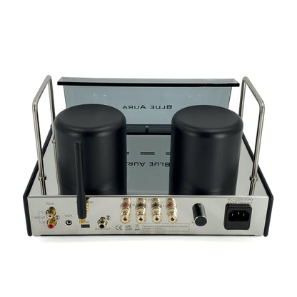 Official high-angle rear three-quarter studio view of the Blue Aura v50 hybrid valve amplifier at rest, showcasing its twin black transformer covers, vertical Bluetooth antenna, and gold-plated speaker terminals.