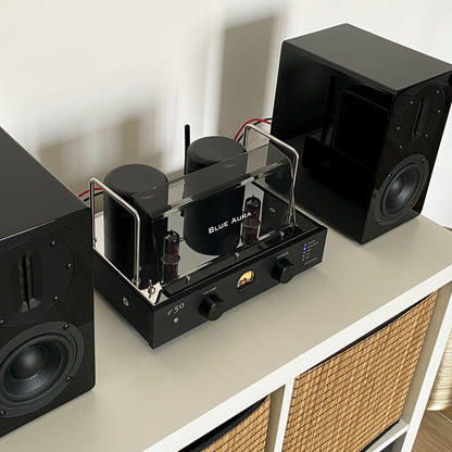 Blue Aura v50 valve amplifier turned on and placed on a white shelf.